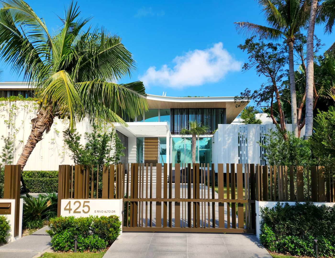 A single storey Miami house behind palms in hard afternoon sun.